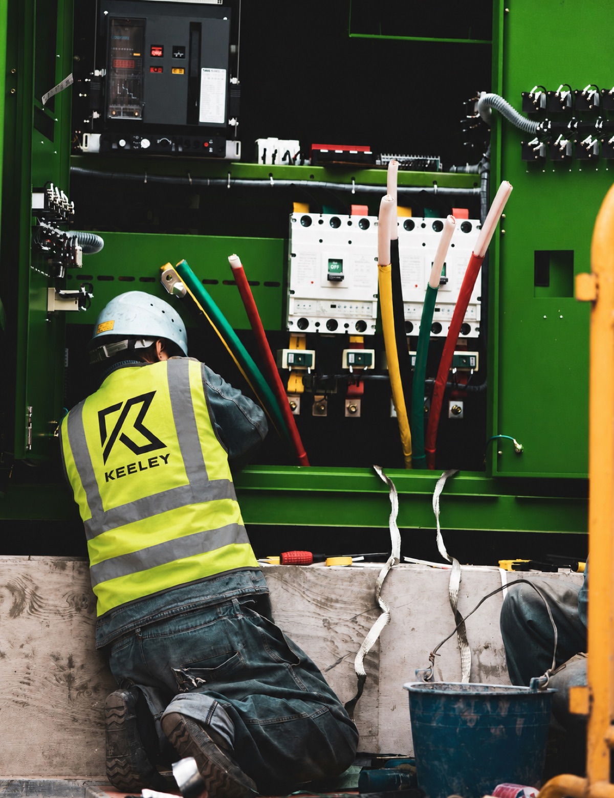 Keeley electrician in a branded safety vest terminating cables inside industrial switchgear