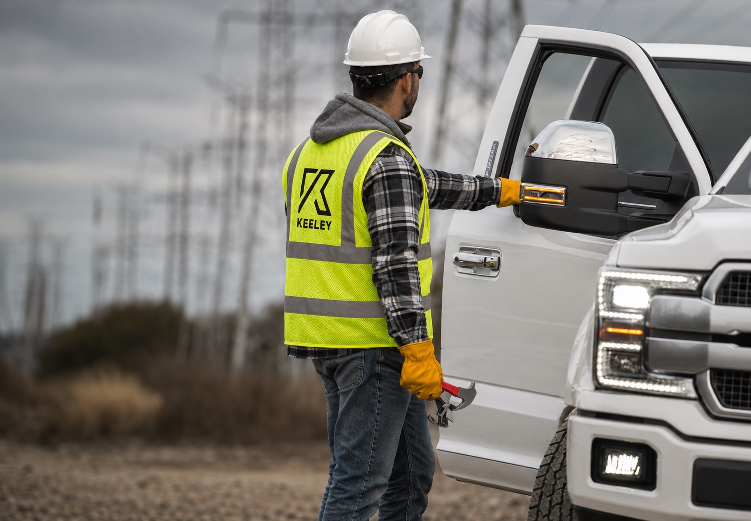 Keeley electrician in branded safety vest and hard hat at a work truck near transmission towers